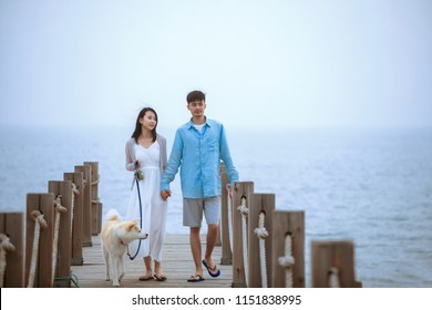 Young Asian Couple Walking On Pier With Pet Dog.