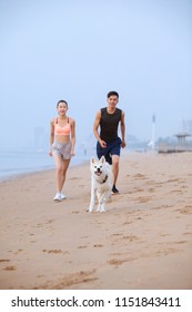 Young Asian Couple Walking On Beach With Pet Dog.