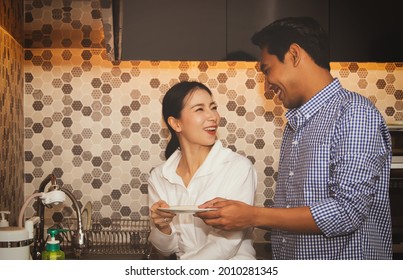 Young asian couple washes dishes in the kitchen at the counter after breakfast : Couple's shared happiness with the chores of washing clean dishes in the modern kitchen at home.