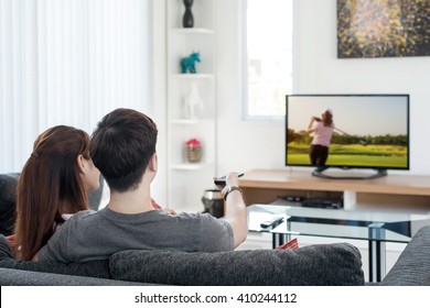 Young Asian couple watching golf sport on tv at home. Enjoy golf sport game.