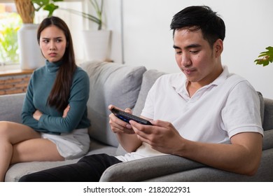 Young Asian couple in which the man plays the game and ignores his wife. His wife's face was filled with indignation.