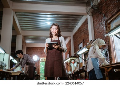 Young asian craftswoman smiling using digital tablet in leather workshop - Powered by Shutterstock