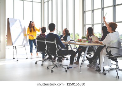 Young Asian Creative Hipster Female Leader Standing And Making Presentation At Modern Office Happy Talking Marketing Idea With Team. Casual Asian People Business Meeting Workshop Soft Tone Concept.