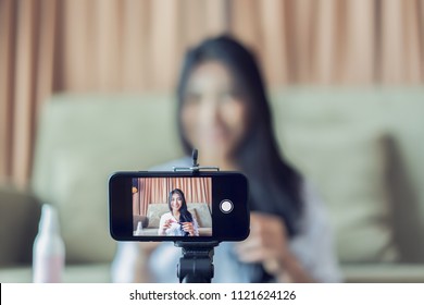 Young Asian cute artist woman beauty vlogger or blogger doing a cosmetic makeup tutorial vlog with brushes looking camera smartphone,recording viral clip share on social media live streaming Internet - Powered by Shutterstock