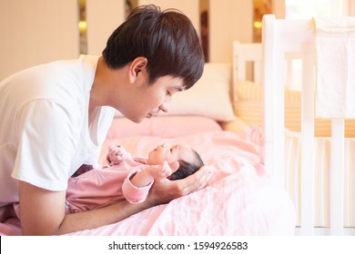 Young Asian Dad  Playing With His  Newborn Baby On The Bed