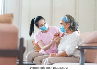 Young Asian Daughter Wearing Surgical Face Mask To Her Mother Sitting In Living Room At Home. Online Learning On Laptop Computer. Protect Against Coronavirus