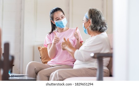 Young Asian Daughter Wearing Surgical Face Mask To Her Mother Sitting In Living Room At Home. Online Learning On Laptop Computer. Protect Against Coronavirus