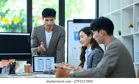Young Asian developer presents mobile app UI UX wireframes and code to colleagues in a collaborative office brainstorm session, ideal for tech and startup concepts.
