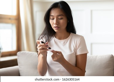 Young Asian Diabetes Patient Woman Sit On Couch Pinch Finger Measure Blood Sugar Level At Home, Millennial Vietnamese Girl Do Daily Checkup Test Glucose With Glucose Meter, Diabetes Problem Concept