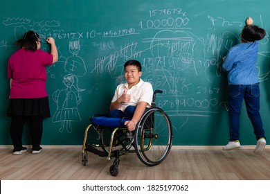 Young Asian Disabled Boy Without Legs Sitting On A Wheelchair, Smile And Looking To Camera While His Friend Fun With Playing And Writing On Green Wall In Classroom. Idea For Handicapped Kid Studying.