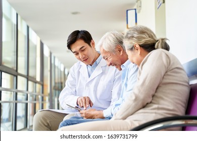 young asian doctor discussing test result and diagnosis with senior couple patients using digital tablet in hospital hallway