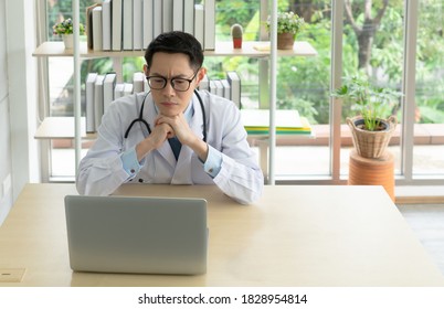 Young Asian Doctor With Seirous Face Using Computer In Hospital Office. Healthcare And Medical Concept