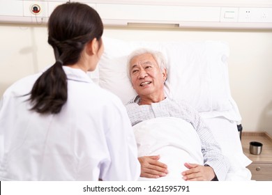 Young Asian Doctor Talking To Senior Patient At Bedside In Hosptial Ward