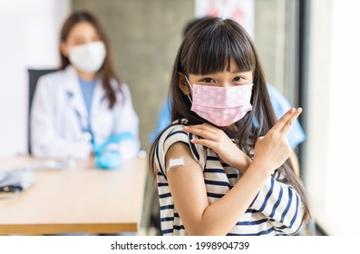 Young Asian Doctor Wearing Gloves And Isolation Mask Is Making A COVID-19 Vaccination In The Shoulder Of Child Patient  At Hospital.