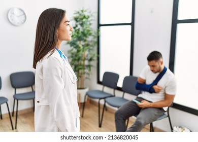 Young Asian Doctor Woman At Waiting Room With A Man With A Broken Arm Looking To Side, Relax Profile Pose With Natural Face With Confident Smile. 