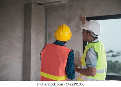 Young Asian engineer or building inspector checking interior building detail with male construction worker by using check list and drawing. Two building worker inspecting interior building.