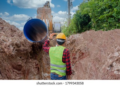 A young Asian engineer is inspecting a large sewer that is buried underground at a construction site. The excavator is empty the water pipe.