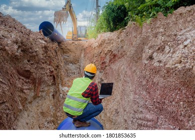 A young Asian engineer is inspecting a large sewer that is buried underground at a construction site. The excavator is empty the water pipe.
