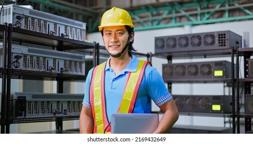 Young Asian Engineer Smiling At Camera With Laptop On His Hand In Crypto Mining Farm Factory