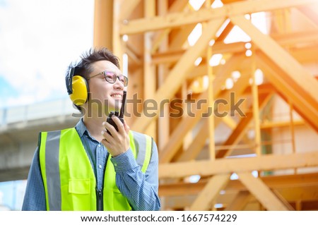 Young asian engineers are working on the construction site. Wear a yellow earmuff sound protection and uniform staff. Hand holding portable radio transceiver for communication