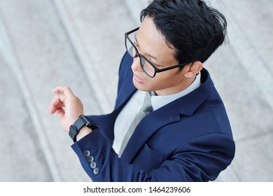 Young Asian Entrepreneur In Glasses Checking Notification On His Smartwatch, View From Above