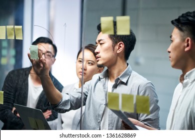 young asian entrepreneur of small company putting a adhesive note on glass in office during team meeting formulating business strategies.