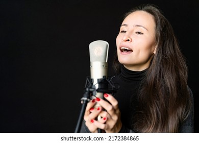 Young Asian Or European Beautiful Brunette Woman Holding Mic, Singing Song To Microphone Alone In Music Studio Or Concert Stage On Black Background. Recording Voice To New Album, Hobby, Education