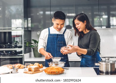 Young Asian Family Couple Having Fun Cooking Together With Baking Cookies And Cake Ingredients On Table.Happy Couple Looking To Preparing The Dough In Kitchen
