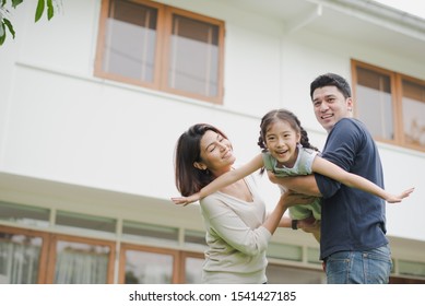 Young Asian Family Love, Father Mother And Daughter Standing Playing And Fun At Outdoor In Front Of Home. Girl And Parent Looking At Camera Which Smiling And Felling Happy. Background Is White House. 