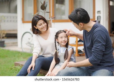 Young Asian Family Love, Father Mother And Daughter Sitting Talking Smiling At Grass Outdoor In Front Of Home. Girl Looking At Father Which Smiling And Felling Happy. Background Is White House. 