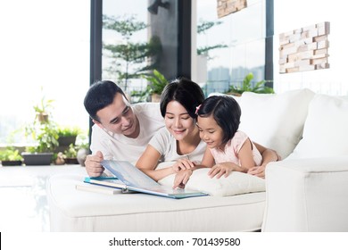 Young Asian Family Reading A Book With Daughter At Home.