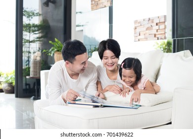 Young Asian Family Reading A Book With Daughter At Home.