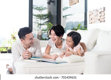 Young Asian Family Reading A Book With Daughter At Home.