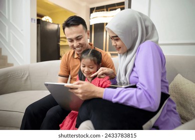 Young Asian family relaxing with a digital tablet sitting on the comfortable sofa, watching video, playing game, have fun together. Education, happines, entertainment concept. - Powered by Shutterstock