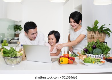 Young Asian Family Using A Laptop While Preparing Meal.