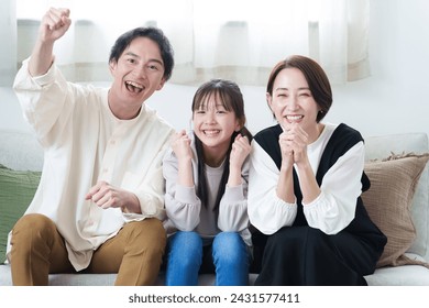 young asian family watching sports game together sitting on sofa in living room