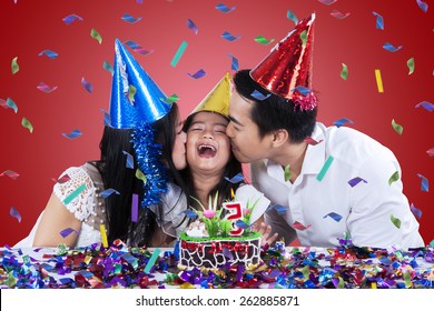 Young Asian Family Wearing Birthday Cap And Kissing The Child In Birthday Party