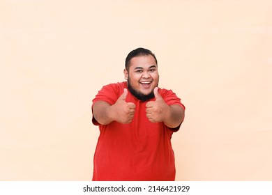 Young Asian Fat Man Wearing Red T Shirt Isolated Background Smiling With Happy Face Looking And Pointing To The Side With Thumb Up.