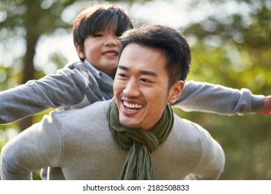young asian father carrying son on back having fun enjoying nature outdoors in park - Powered by Shutterstock
