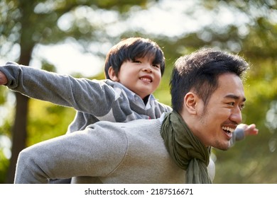 young asian father carrying son on back having fun enjoying nature outdoors in park