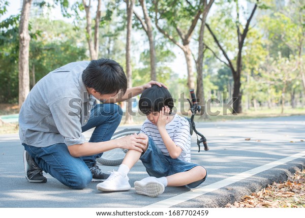 Young\
asian father of dad calms son that fell from the bike and he get\
injury on knee and leg while have weekend leisure in public\
park,accident can happen everywhere and every\
time.