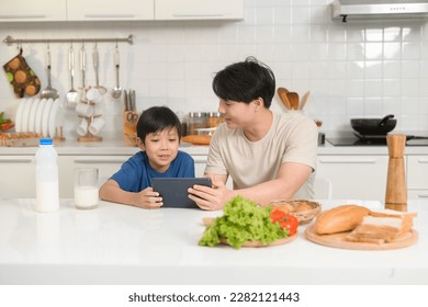 Young Asian father and his son using digital tablet enjoying together in kitchen at home - Powered by Shutterstock