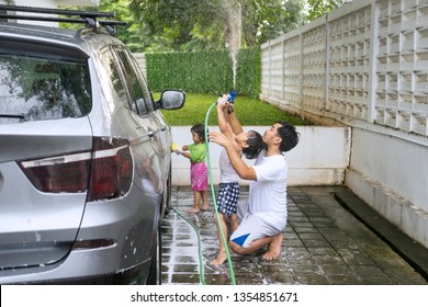 Young Asian Father Washing A Car With His Children At Home While Using A Water Hose And Sponge 