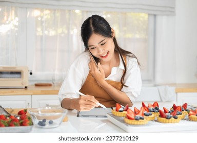 Young asian female Business owner in apron using laptop and talking to clients on the phone by workplace.Organization of Work in the Field of Delivery.selling bakery online. - Powered by Shutterstock