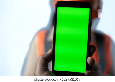 Young Asian female construction worker shows green screen of cell phone to camera, industrial and construction advertising concept, isolated on white background. - Powered by Shutterstock