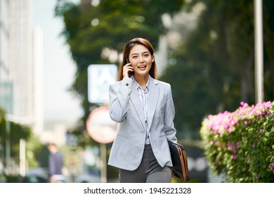 young asian female corporate executive talking on cellphone while walking in city street