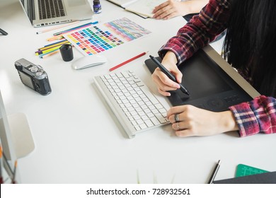 Young asian female designer using graphics tablet while working with computer at studio or office.
