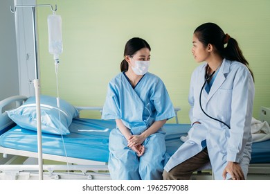 Young Asian Female Doctor With Patient Wearing Surgical Face Mask Sitting On Hospital Bed Talking To Each Other And Talking Routine Status Update