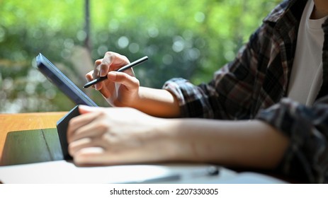 Young Asian Female In Flannel Shirt Remote Working At The Coffee Shop, Using Portable Tablet To Manage Her Tasks. Cropped And Rear View Image