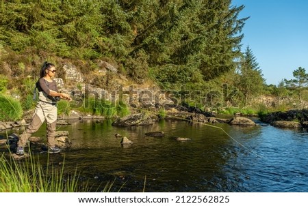 A young asian female fly fishing on a river on a summers evening